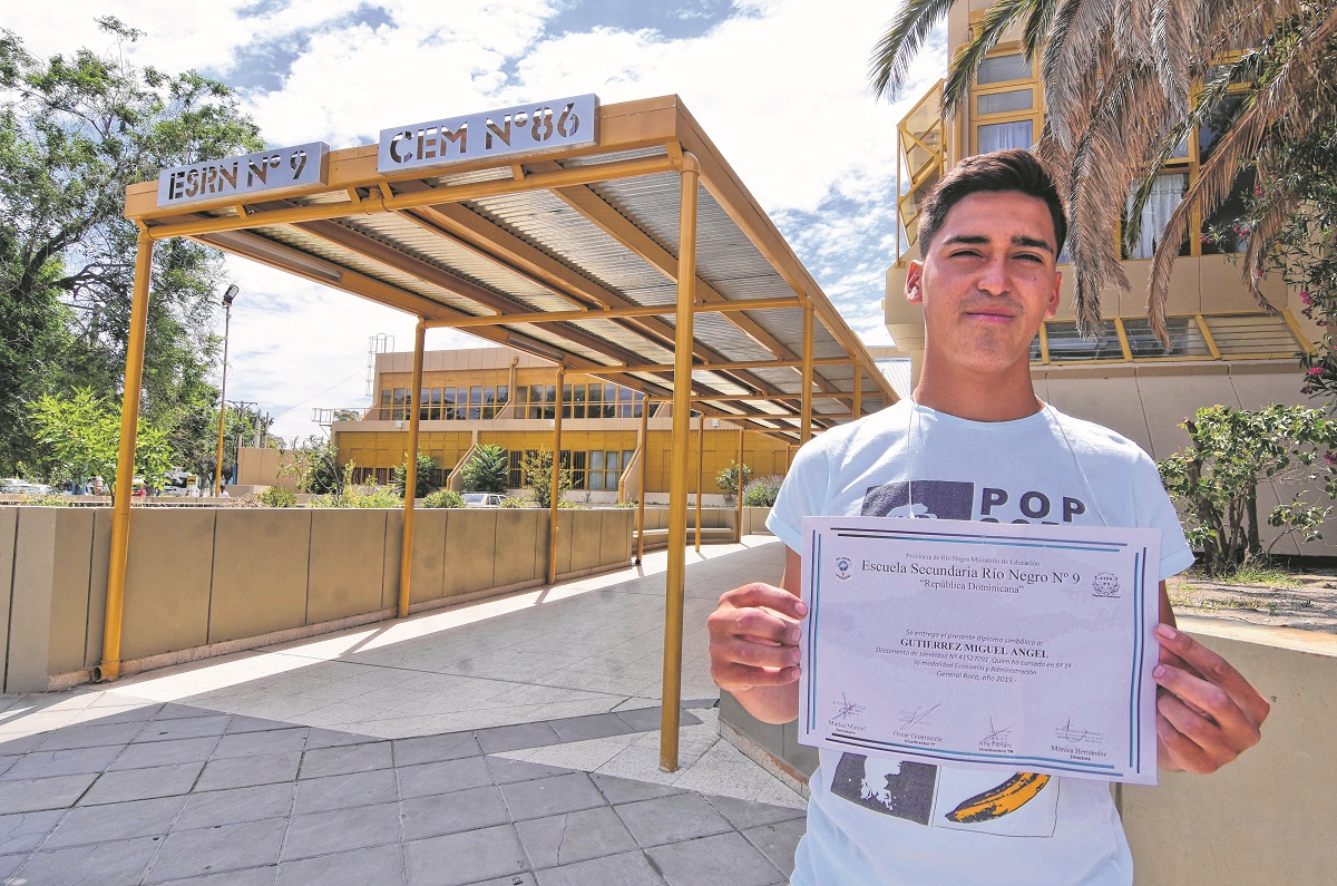 Miguel Angel Gutierrez, con diploma en mano en la fachada de su colegio, la ESRN N° 9.
