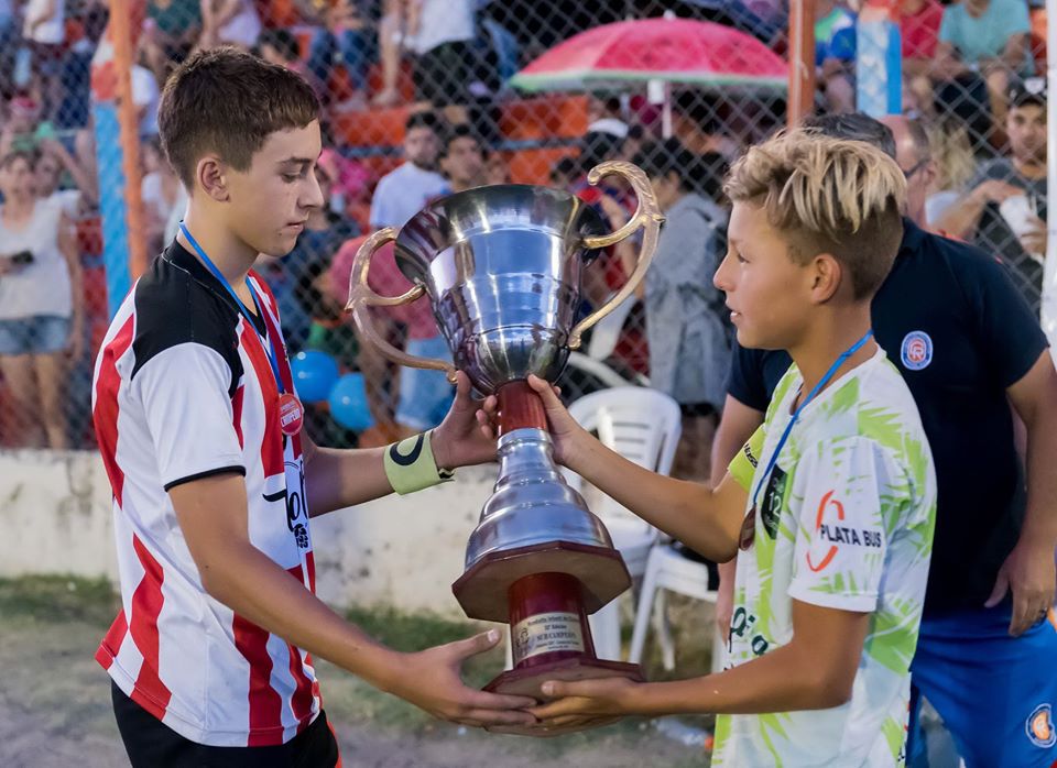 El capitán de campeón 12 de Marzo (La Plata) le entrega la copa del 2° puesto a su colega de Buena Parada de Río Colorado. Los valores de la amistad deportiva, por encima de la competencia.