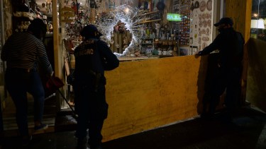 Policías de la Comisaría Segunda bajo la lluvia intentaban tapar la vidriera dañada en la calle Mitre de Bariloche. Foto: Alfredo Leiva