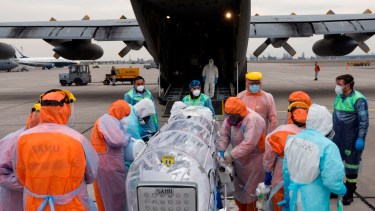 Personal sanitario de la Fuerza Aérea de Chile (FACH) e integrantes del Servicio de Atención Médica de Urgencia SAMU (de naranja) llevan a un avión a un paciente crítico de COVID-19, en Santiago. Foto: EFE/Alberto Valdés