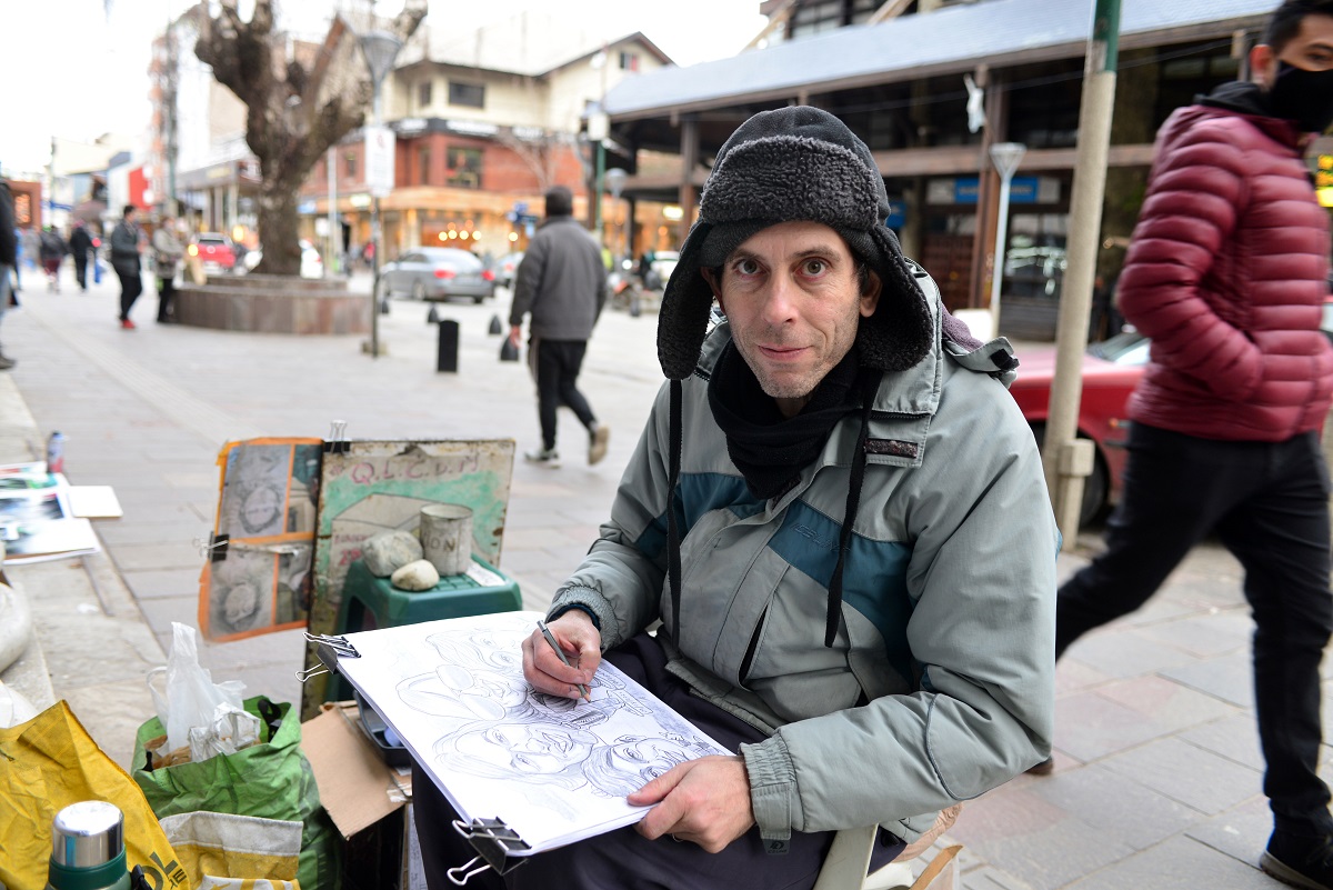 Es duro el invierno, pero todas las tardes Cristian Valverde instala su atelier en la vereda del banco Nación para que los turistas compren sus caricaturas. Foto: Chino Leiva