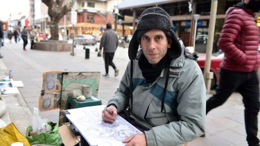 Es duro el invierno, pero todas las tardes Cristian Valverde instala su atelier en la vereda del banco Nación para que los turistas compren sus caricaturas. Foto: Chino Leiva
