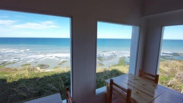 La confitería y restaurante se encuentra sobre el acantilado y de fondo se observa las restingas y pozones naturales de la playa La Lobería.
