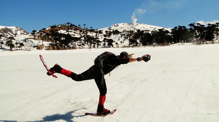 Flavio con sus raquetas de nieve sobre la laguna Escondida congelada por completo en Caviahue Copahue, con las araucarias y la fumarola del volcán de fondo en la cordillera neuquina. Foto: De la Patagonia al Mundo.