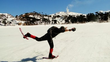 Flavio con sus raquetas de nieve sobre la laguna Escondida congelada por completo en Caviahue Copahue, con las araucarias y la fumarola del volcán de fondo en la cordillera neuquina. Foto: De la Patagonia al Mundo.