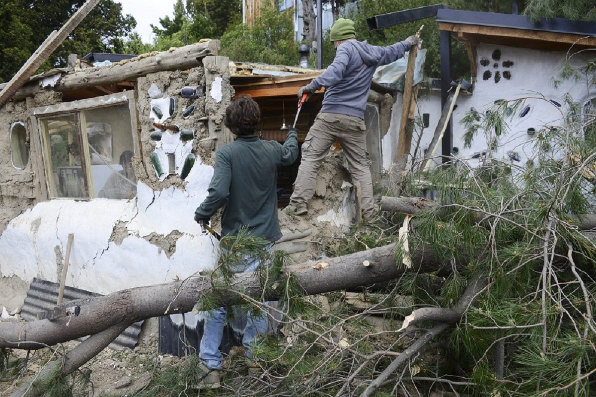 Dos vecinos ayudan a retirar el árbol que cayó y destruyó su casa, en el barrio Pilar de Bariloche. Foto: Chino Leiva