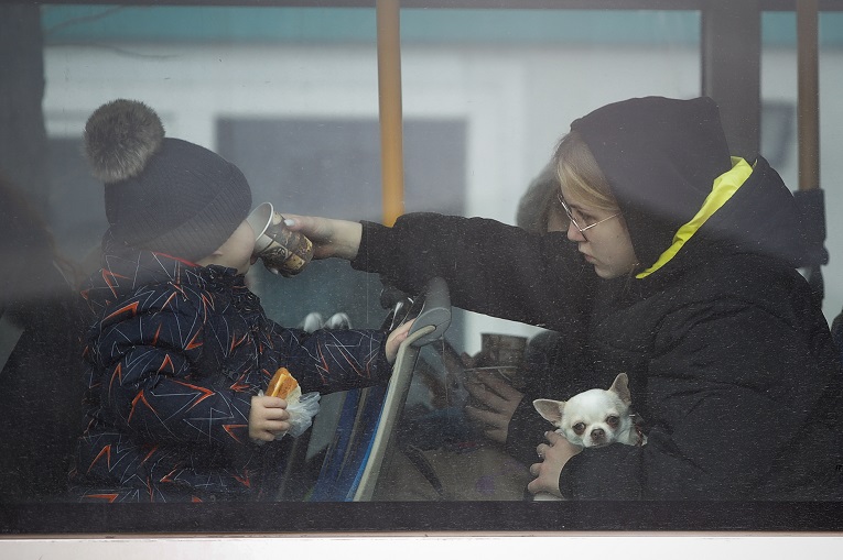 Una refugiado le da un sorbo de té a un niño mientras sostiene un perro pequeño, mientras huye del conflicto en un autobús en la frontera rumano-ucraniana, en Siret, Rumania. (AP Photo/Andreea Alexandru)