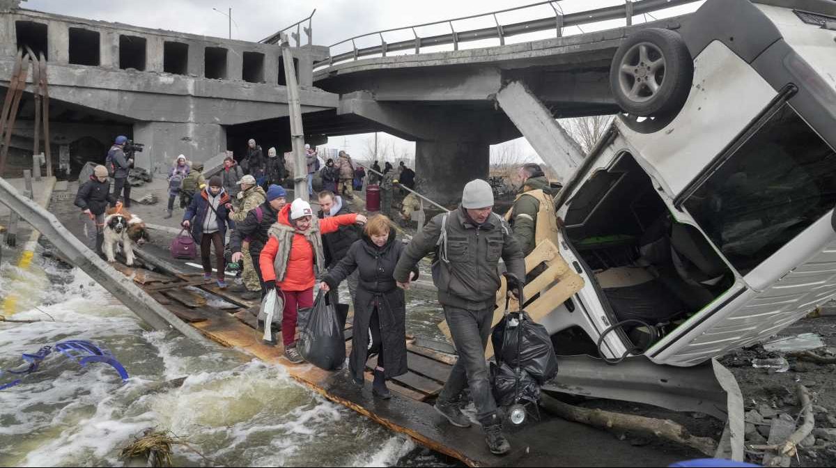 Las personas cruzan un camino improvisado debajo de un puente destruido mientras huyen de la ciudad de Irpin cerca de Kiev. (Foto AP/Efrem Lukatsky)