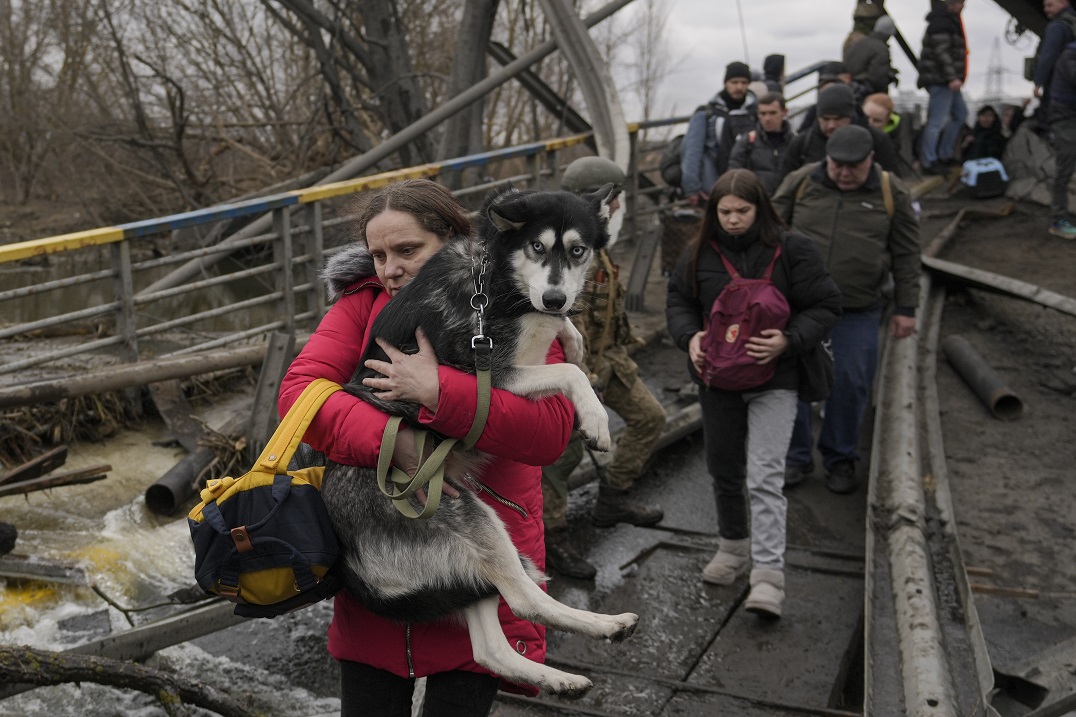 Una mujer sostiene a un perro mientras cruza el río Irpin en un camino improvisado debajo de un puente mientras la gente huye de la ciudad del mismo nombre. (AP Photo/Vadim Ghirda)