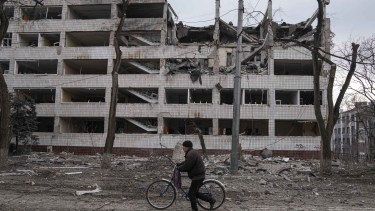A man walks with a bicycle in front of a damaged by shelling in Mariupol, Ukraine, Thursday, March 10, 2022. (AP Photo/Evgeniy Maloletka)