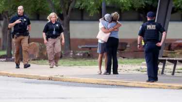 Dos personas se abrazan afuera de Memorial High School, donde las personas fueron evacuadas de la escena de un tiroteo en el edificio médico Natalie el miércoles  (Ian Maule/Tulsa World via AP)