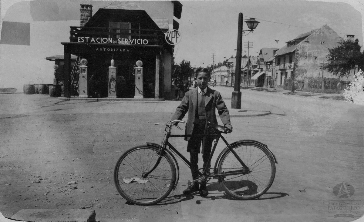  Juan Hegoas, sostiene la bicicleta en los años '50 en la tradicional calle Mitre de Bariloche. Colección Pizzuti en Archivo Visual Patagónico.