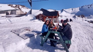 Turistas disfrutan del solcito y la nieve mientras toman algo en Copahue. Detrás, el refugio El Montañés, abierto este invierno en la villa termal neuquina. 