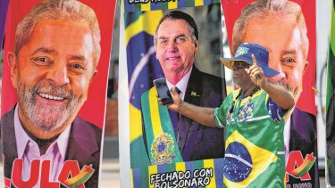 Un manifestante vestido con los colores de la bandera brasileña camina frente a unas toallas de un vendedor ambulante que muestran a los candidatos presidenciales brasileños, el actual presidente Jair Bolsonaro (centro) y el expresidente Luiz Inácio Lula da Silva, en Brasilia, el martes 27 de septiembre de 2022. (AP Foto/Eraldo Peres)