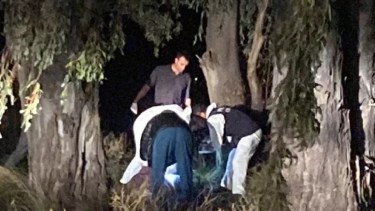 La policía científica trabajó sobre el monte de eucaliptos durante la noche del lunes. Aún no se logró identificar al hombre brutalmente asesinado y descartado en la ruta nacional 3. Foto Gentileza: La brújula. 