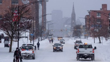Personas y vehículos se mueven por Main St. en Buffalo, Nueva York, después de que una gran tormenta de nieve cubriera la ciudad. Junto con las derivas y las prohibiciones de circulación, muchas calles quedaron intransitables debido a los vehículos abandonados. AP Photo - Craig Ruttle
