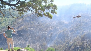 Un helicóptero sobrevuela el cerro incendiado en El Hoyo y un turista de cerca registra su tarea. Foto: Chino Leiva