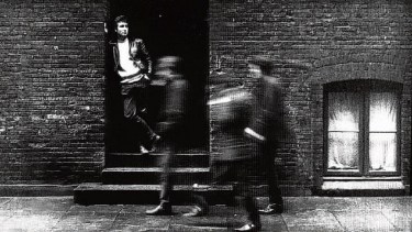 Foto original. Lennon parado en la puerta mirando pasar a los “borrosos” Paul Mc Cartney, George Harrison y Stu Sutcliff. Ese día, Pete Best, baterista de la banda, prefirió hacer otra cosa. Y sí, contaron bien, Los Beatles en aquel tiempo eran cinco.
