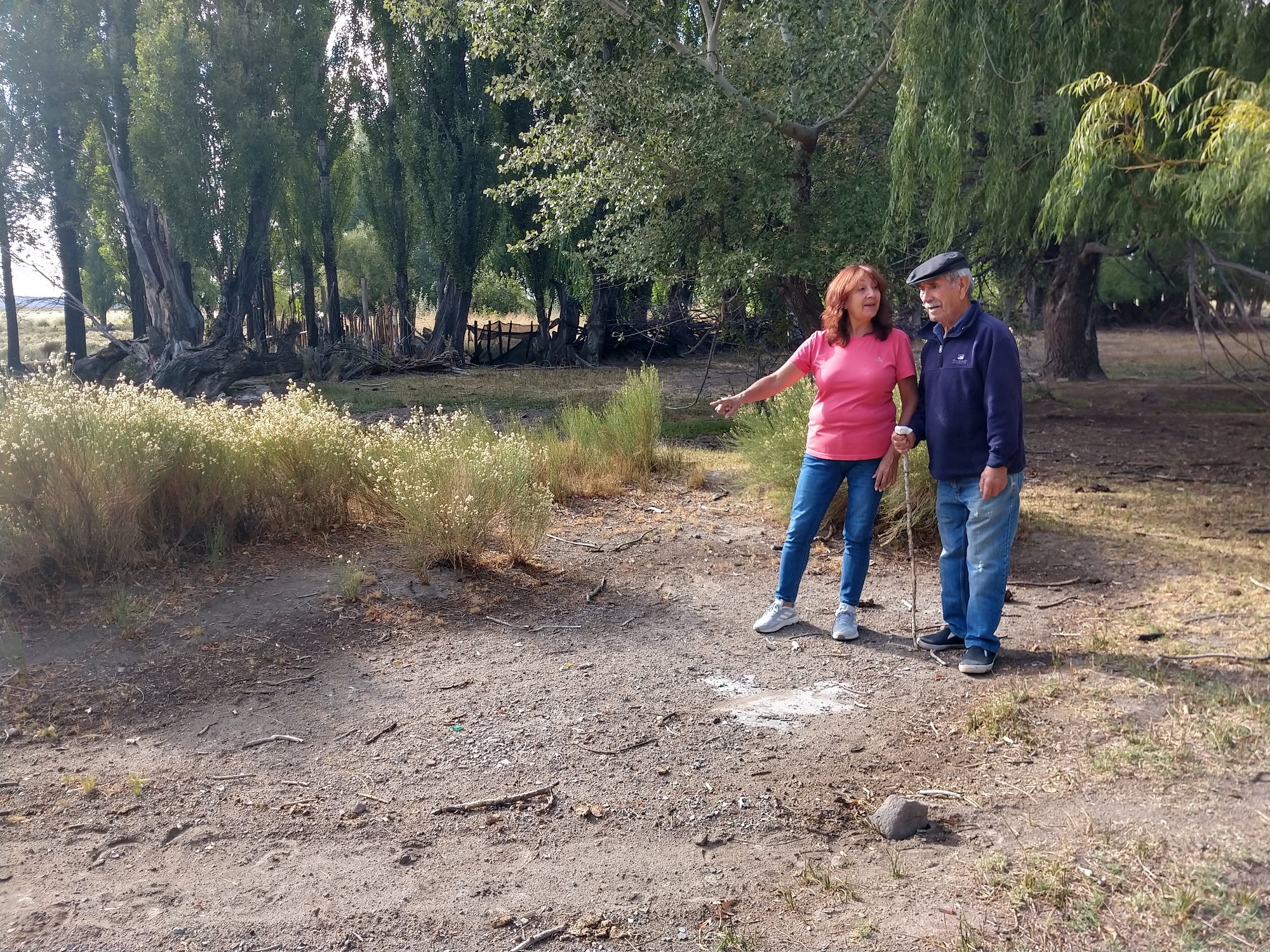 Mónica y Leonel observan el rectángulo de suelo libre, rodeado de pasto, que marcaba el punto donde funcionó el almacén, hecho de adobe. El dato fue ratificado por la Declaración 2250 de la Legislatura neuquina. Foto: Melina Ortiz Campos.