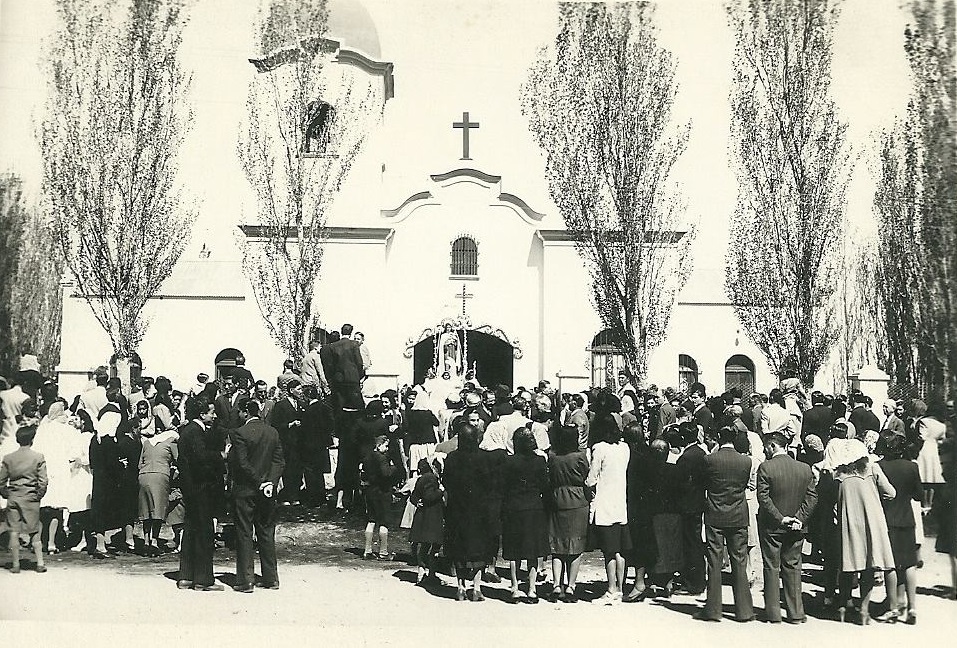 El recuerdo de la parroquia de Plaza Huincul, en la década del '40... los álamos del comienzo y los vecinos luciendo la moda de época. Foto: Facebook. 