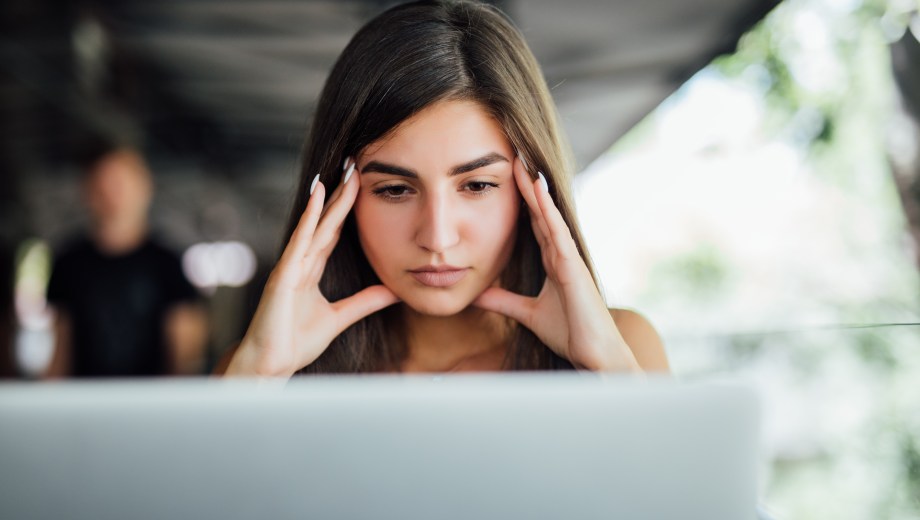 Stressed busy tired young girl in working on her report in front of laptop in the summer cafe