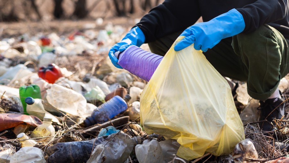 Man in gloves collecting scattered plastic bottles from the ground in the nature